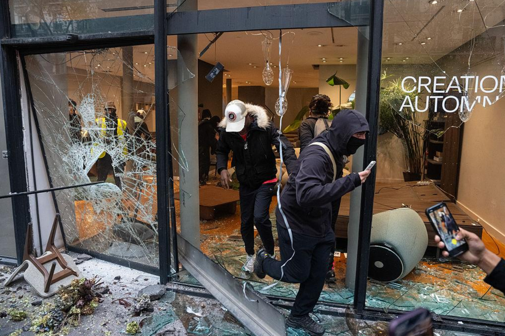 france-riots-2026-paris-protests People gather outside a damaged shop in Paris following disorder during nationwide protests.