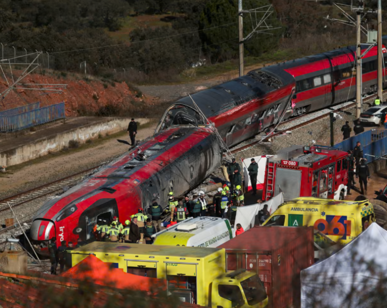 Emergency crews work beside a severely damaged red high-speed train following a derailment. Firefighters and paramedics gather around the carriages, with ambulances and fire engines positioned alongside the railway.